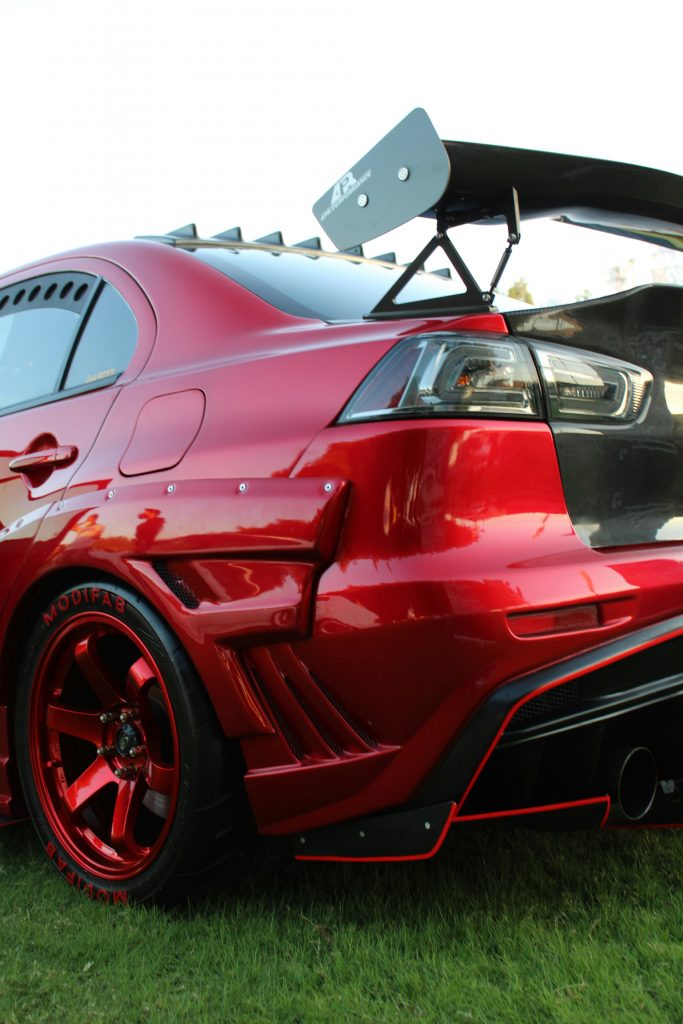 Rear view of a modified red Mitsubishi Lancer Evolution featuring a widebody kit, large rear wing, custom wheels, and aggressive aftermarket styling
