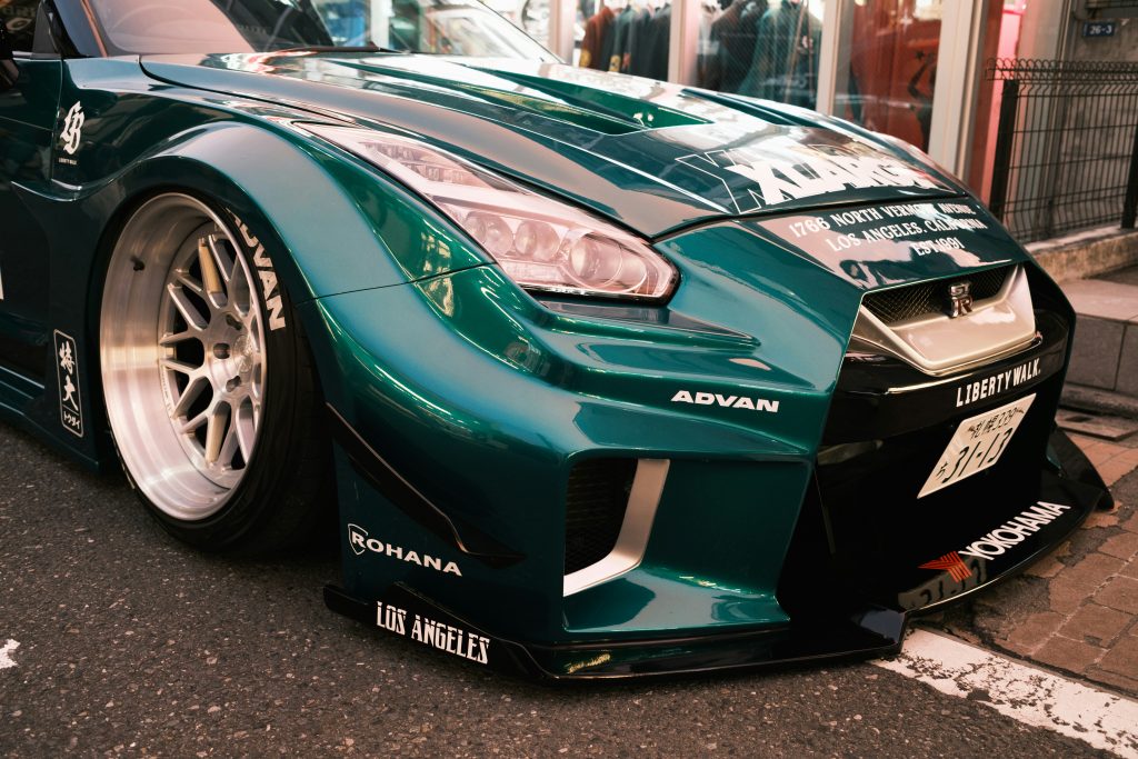Close-up of a modified Nissan GT-R with a widebody kit, custom wheels, and aftermarket front bumper, showcasing a highly customized street build