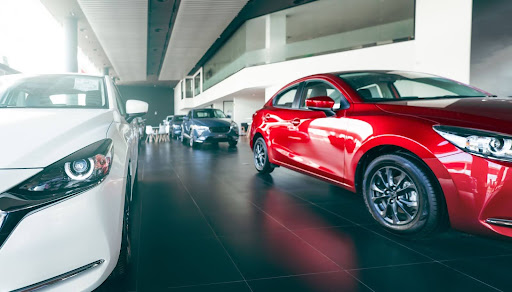 Modern car dealership showroom with a lineup of new vehicles, including a red sedan and a white car in the foreground, displayed under bright lighting