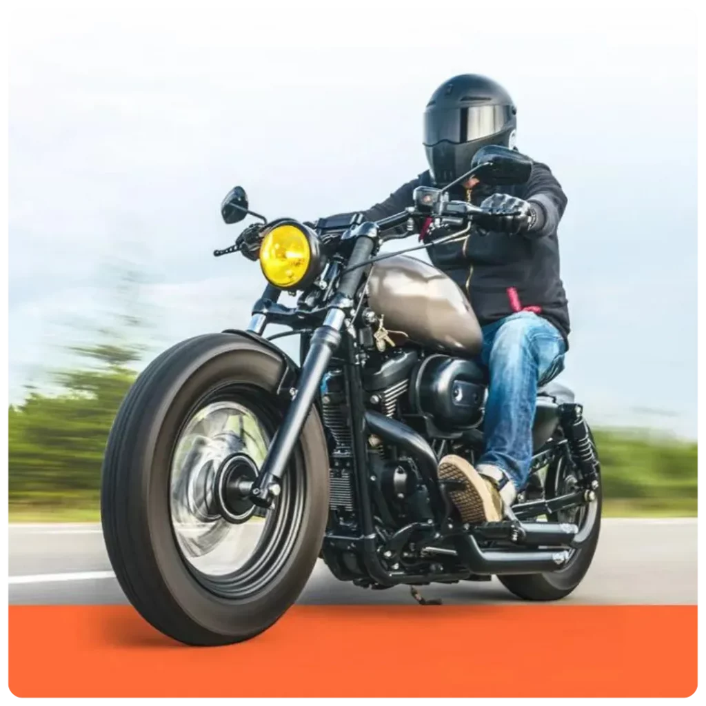 This image shows a motorcyclist wearing a black helmet and jacket riding a custom bobber-style motorcycle with a matte tank and yellow headlight on an open road. - Dirt Legal This image shows a motorcyclist wearing a black helmet and jacket riding a custom bobber-style motorcycle with a matte tank and yellow headlight on an open road.