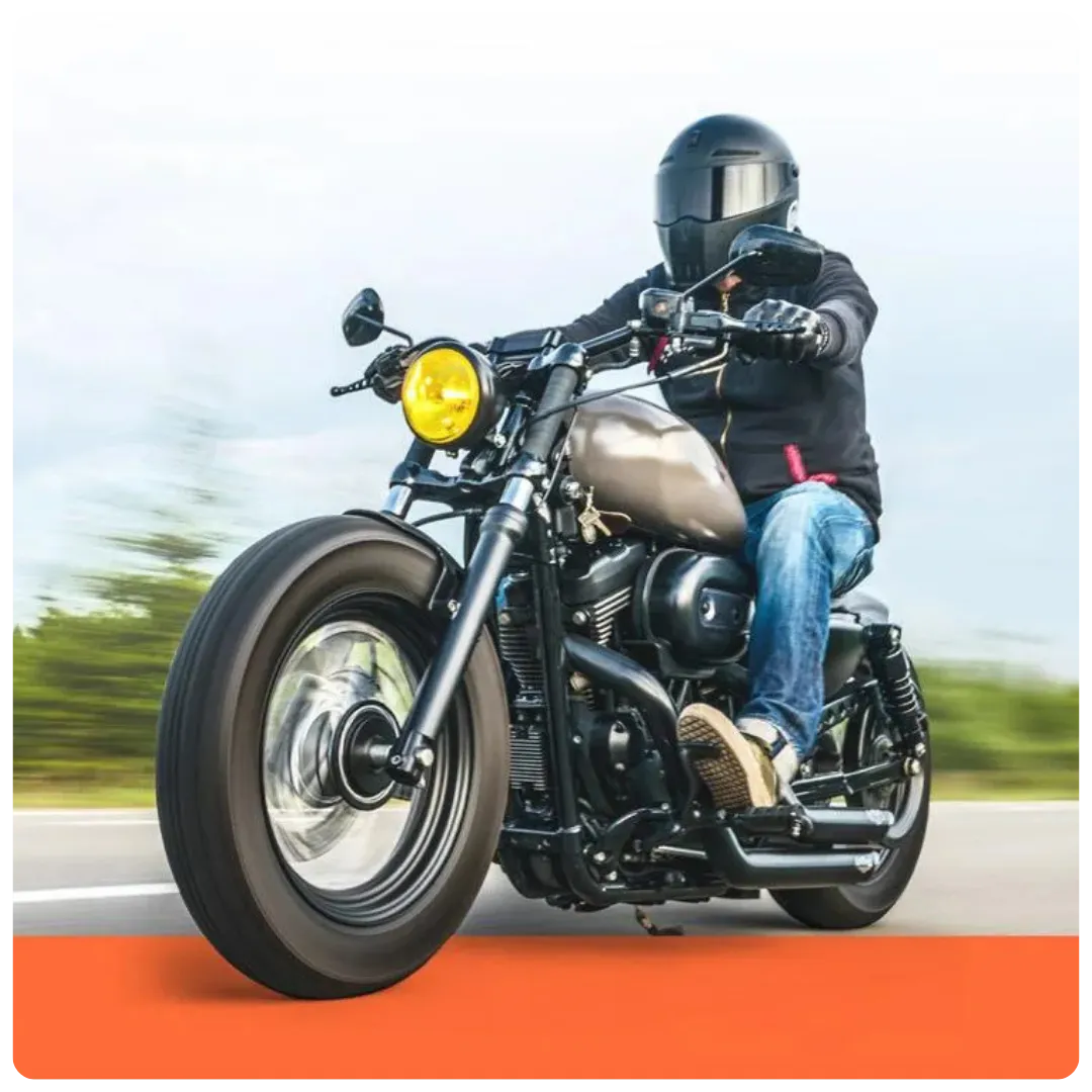 This image shows a motorcyclist wearing a black helmet and jacket riding a custom bobber-style motorcycle with a matte tank and yellow headlight on an open road. - Dirt Legal This image shows a motorcyclist wearing a black helmet and jacket riding a custom bobber-style motorcycle with a matte tank and yellow headlight on an open road.