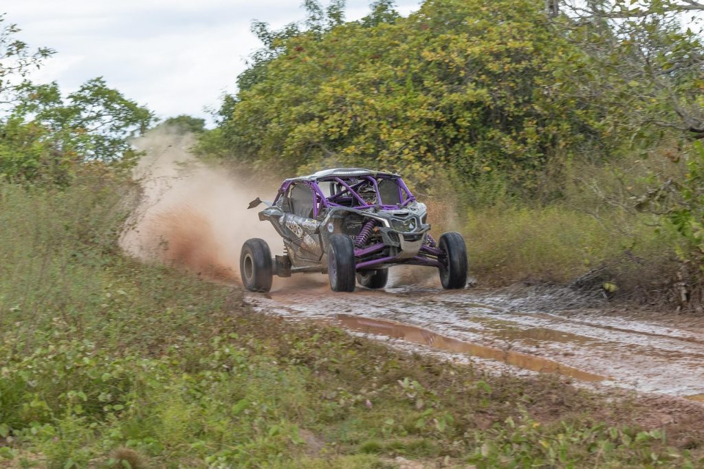 A high-performance off-road UTV kicks up mud and dirt as it speeds down a rugged forest trail.