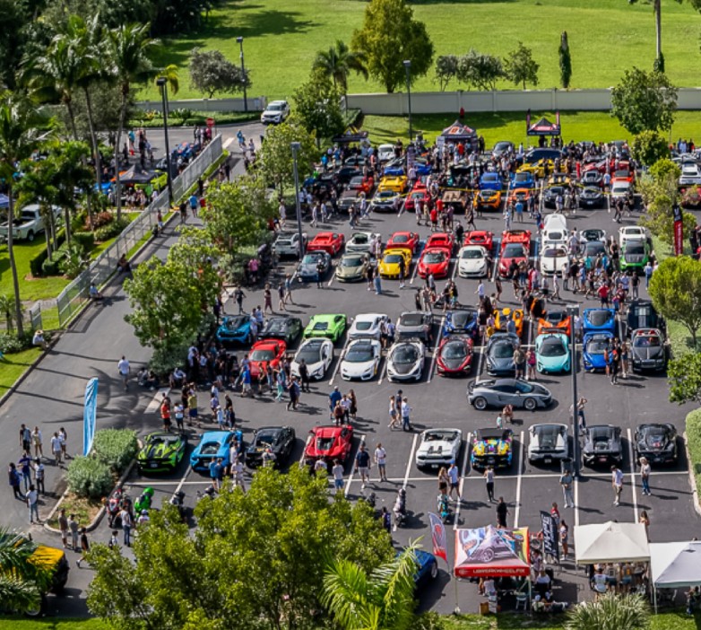 An aerial view captures the vibrant scene at Supercar Saturdays Florida, with rows of exotic cars and crowds filling the parking lot in a lively community gathering.
