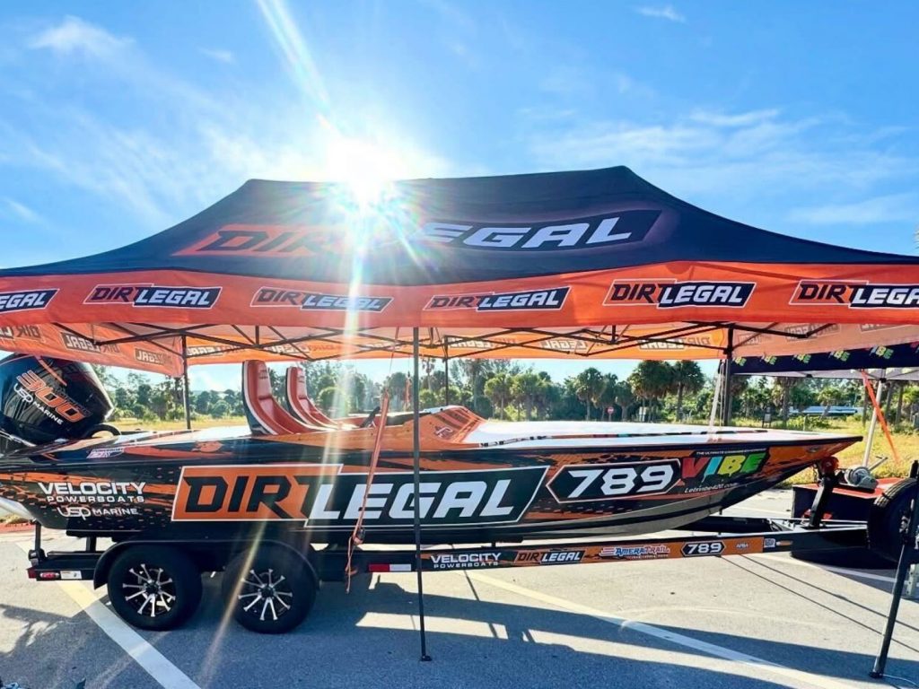 Dirt Legal Tent and Race Boat - Dirt Legal This image shows the Dirt Legal-sponsored Velocity race boat displayed under a branded Dirt Legal canopy, highlighting the team’s presence at offshore racing events.