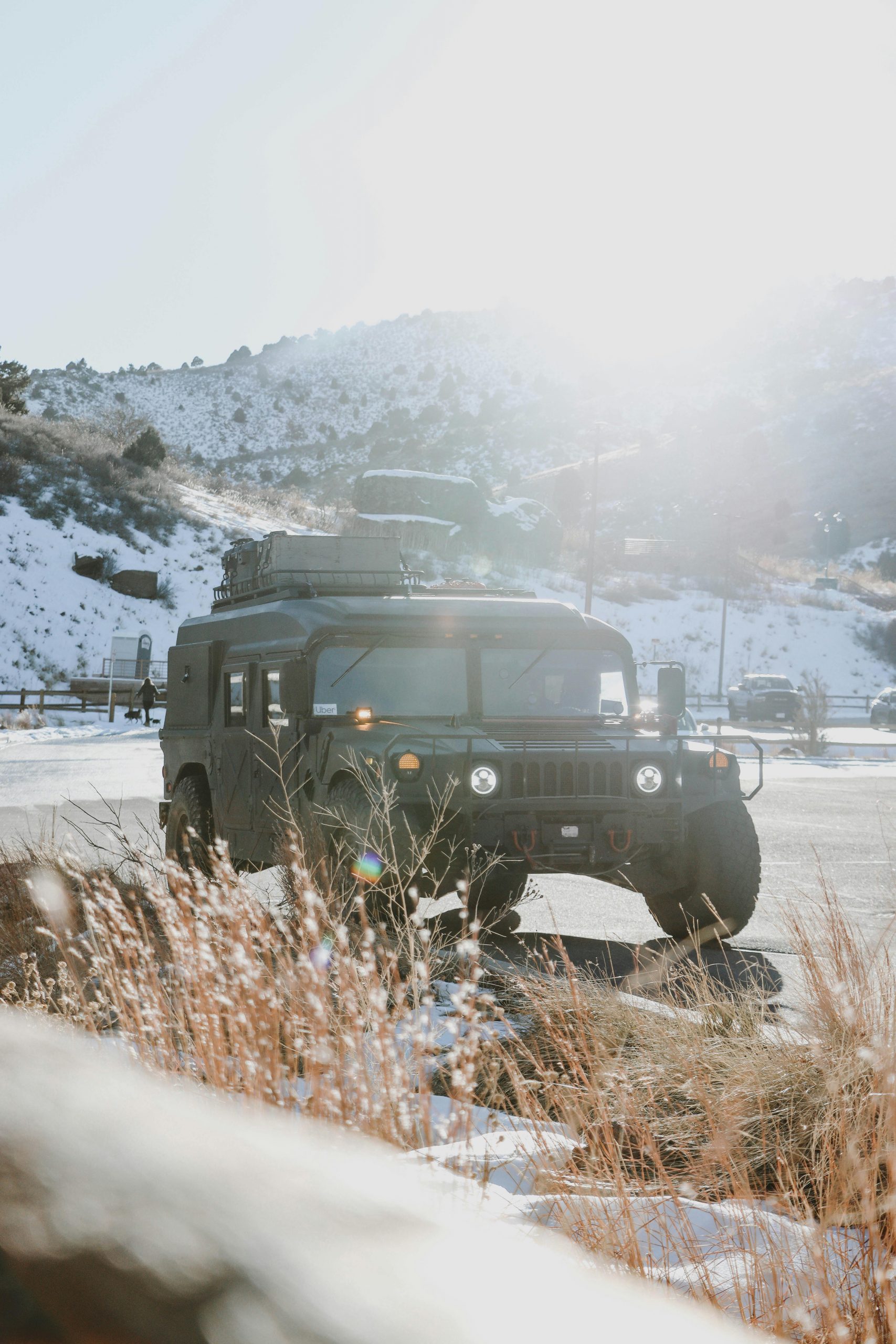 A rugged military Humvee sits on a snowy roadside with mountains in the background, symbolizing the process of registering military trucks through a Montana LLC for legal road use.