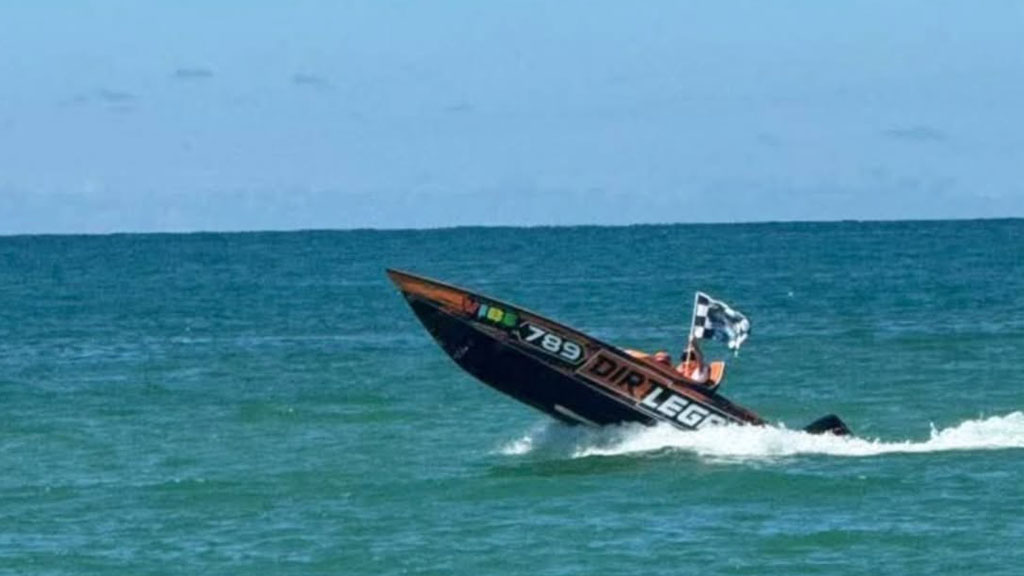 High-Flying Dirt Legal #789 Race Boat on the Ocean - Dirt Legal Orange and black 'Dirt Legal' powerboat, number 789, with a checkered flag visible, dramatically leaping out of the water at high speed against a calm blue ocean backdrop. The boat's bow is pointed upwards as it makes a splash.