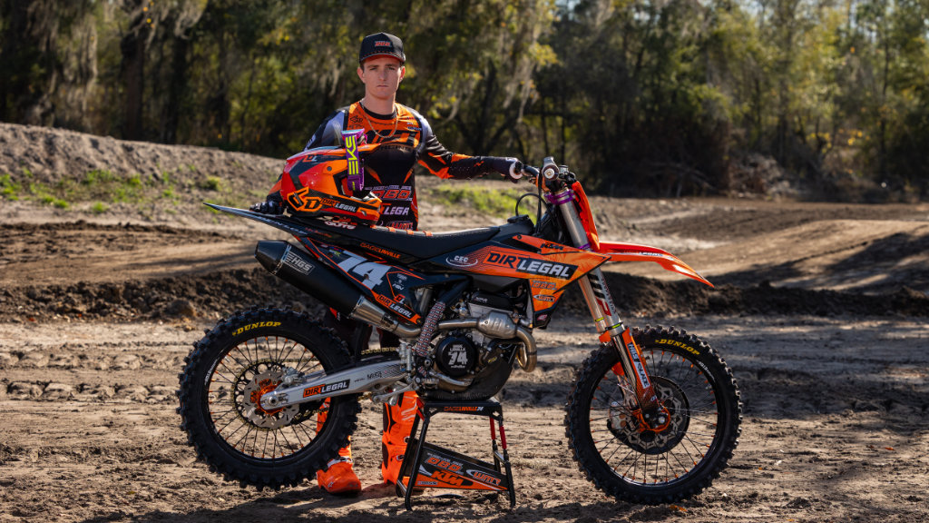 Gage Linville standing with his Dirt Legal DBDRacing WMR KTM race bike on a practice track, showcasing team graphics and sponsors.