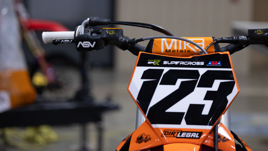 A detailed view of the handlebars and front number plate of Anthony Rodriguez’s KTM dirt bike, featuring ASV levers, Mika Metals bars, and a prominent Dirt Legal logo.