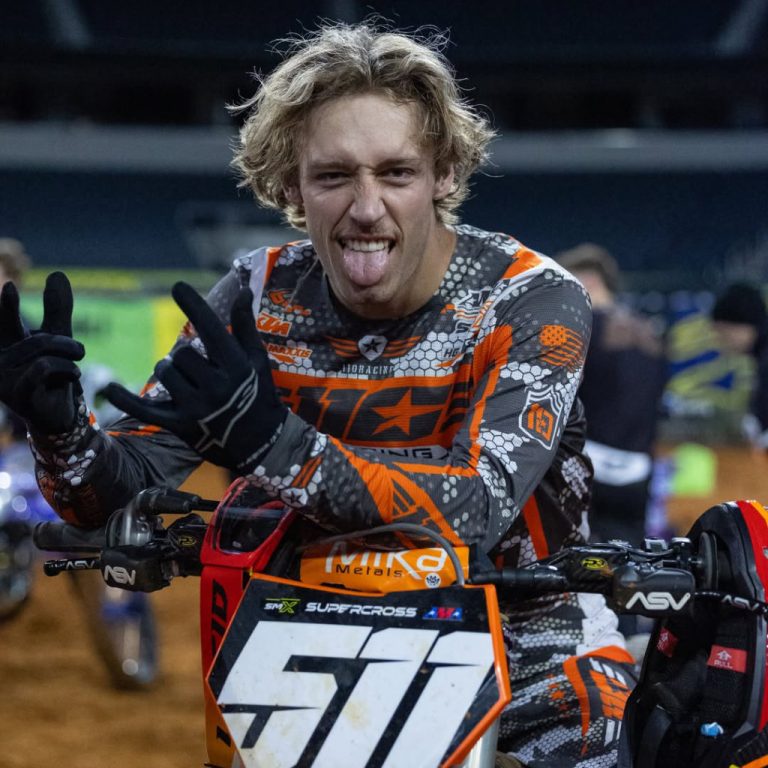 A close-up of Jace Kessler leaning over his #511 KTM handlebars, flashing a tongue-out expression and hand signs. He’s wearing his signature orange and grey 110 Racing x Dirt Bike Depot jersey inside Lucas Oil Stadium.