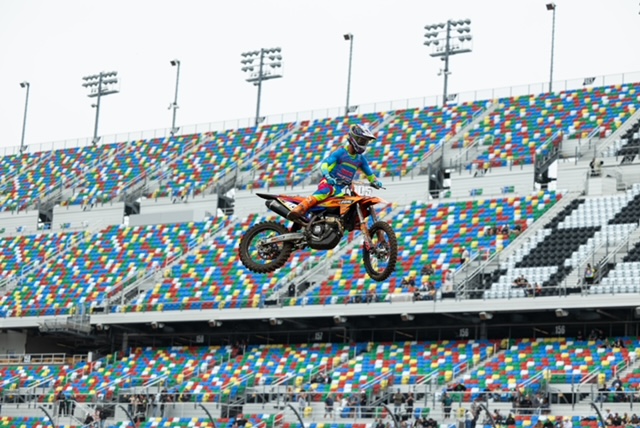 Jace Kessler catching massive air on his KTM dirt bike in front of the iconic colorful grandstands at Daytona International Speedway during qualifying.