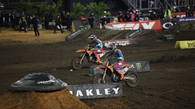 Two Dirt Legal DBD Racing WMR KTM riders, Marcus Phelps and Jace Kessler, competing side-by-side on the Daytona International Speedway track during a night session.