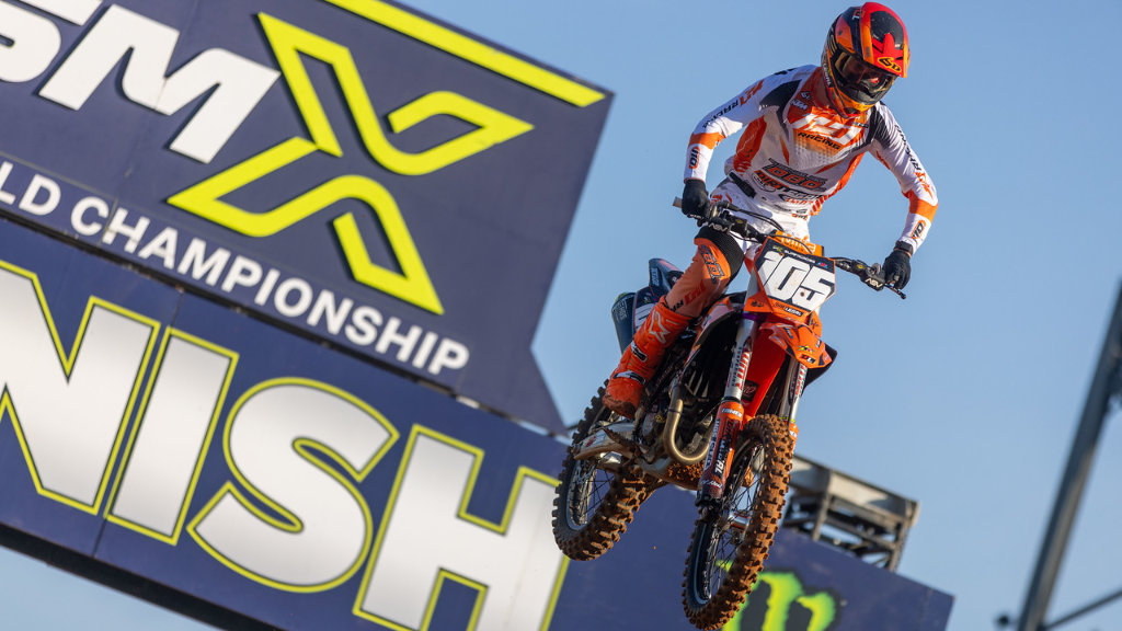 Pro rider Marcus Phelps in white and orange Dirt Legal racing gear performing a jump on his KTM bike in front of a Supercross World Championship finish line sign.