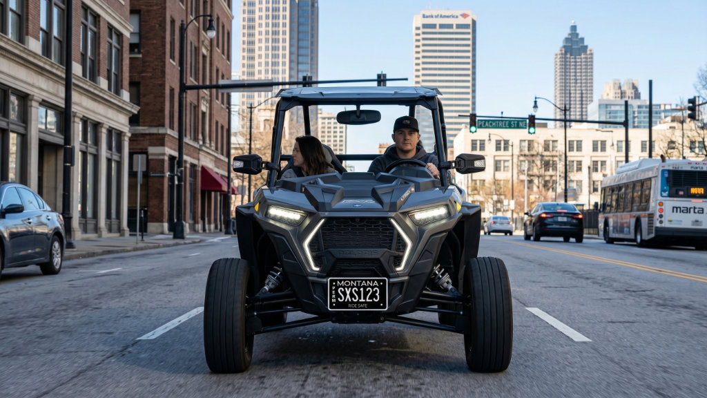 Two people driving a Polaris Slingshot with a Montana license plate through a downtown street in New Jersey, showing a registered side-by-side operating on public roads.