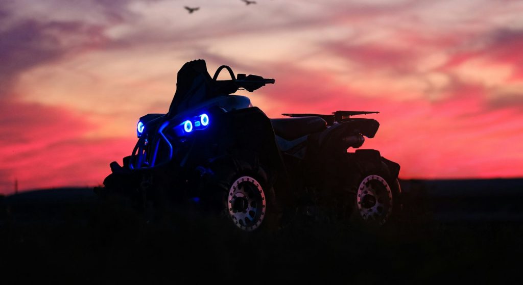 ATV with blue headlights parked on a dark field at sunset
