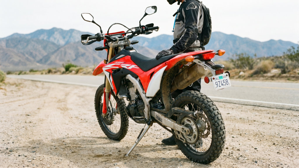 Honda CRF450 Street Legal Conversion - Dirt Legal A red and white Honda CRF450 dirt bike parked on a dirt shoulder next to a paved road. The motorcycle features street-legal modifications including side mirrors, turn signals, and a visible rear license plate. A rider stands next to the bike in a desert mountain landscape.