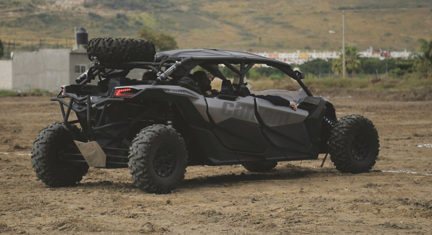 Black Can-Am side by side parked on a dirt lot with off road tires and a mounted spare tire in a rugged outdoor setting
