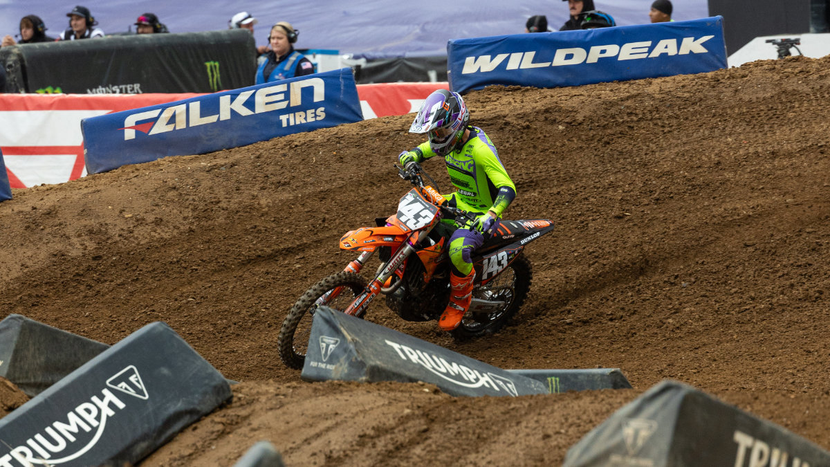 A professional motocross rider maneuvers a Dirt Legal sponsored race bike through a difficult, rutted corner section of a stadium race track.