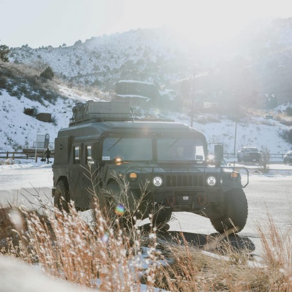 A rugged military Humvee sits on a snowy roadside with mountains in the background, symbolizing the process of registering military trucks through a Montana LLC for legal road use.